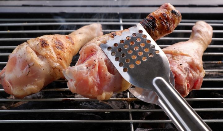 flipping chicken drumsticks on the grill with tongs